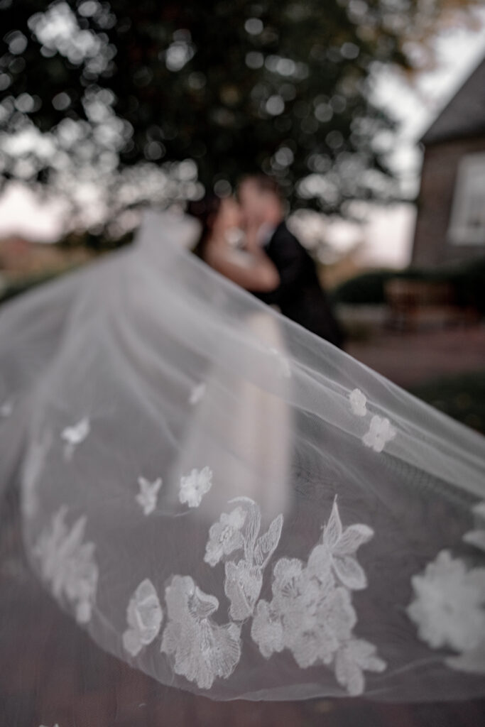 Bride and groom blurred our in background with detail of veil flying in front.