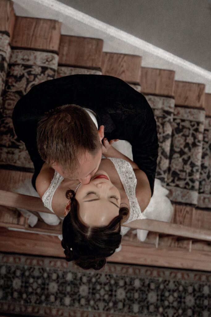 groom kissing brides neck on staircase railing.