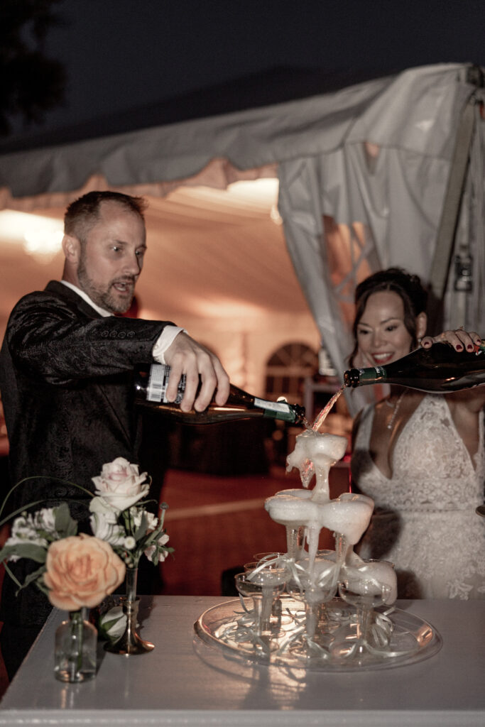 bride and groom pouring two bottles of champagne into champagne tower.