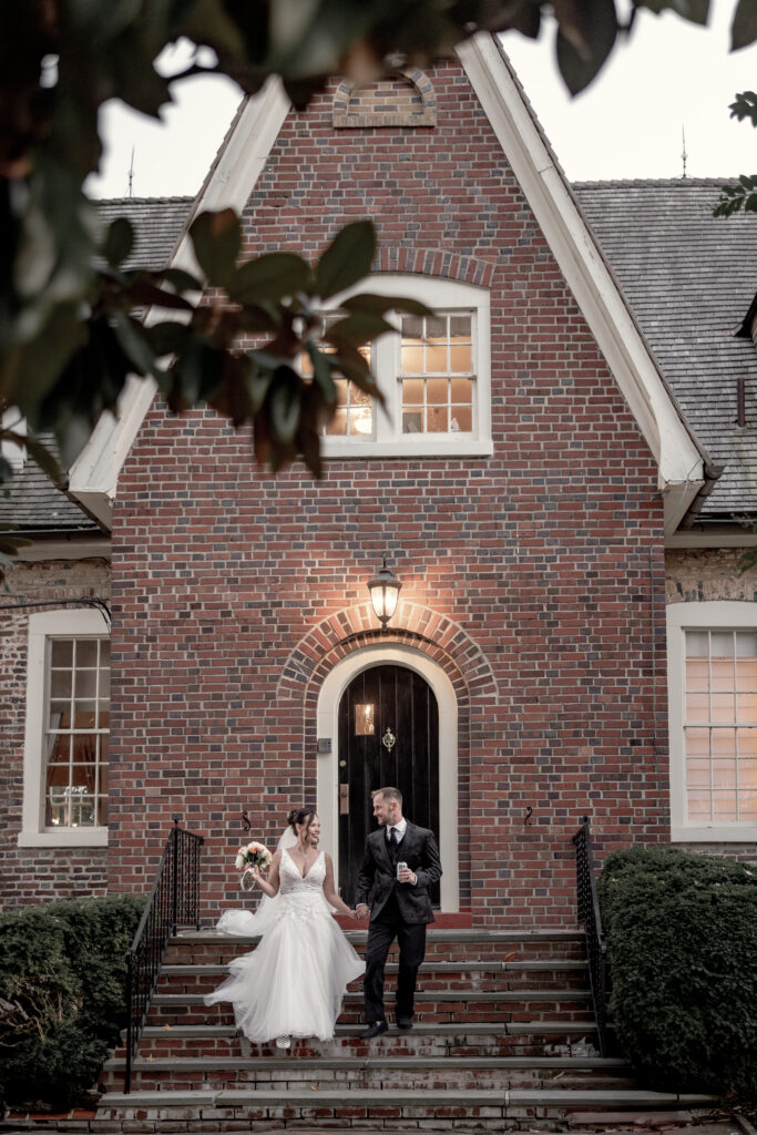 Bride and groom walking down stairs in front of billingsley house manor holding bouquet and a beer.