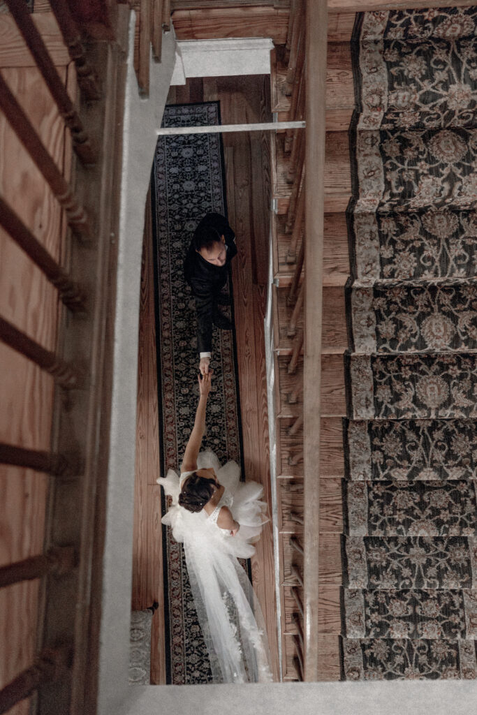 Bride and groom talking down hallway viewed from birds-eye view from opening of staircase.