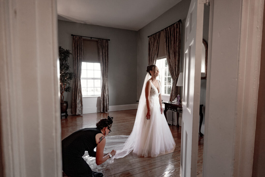 looking through door, bride laughing with her friend fixing her veil.