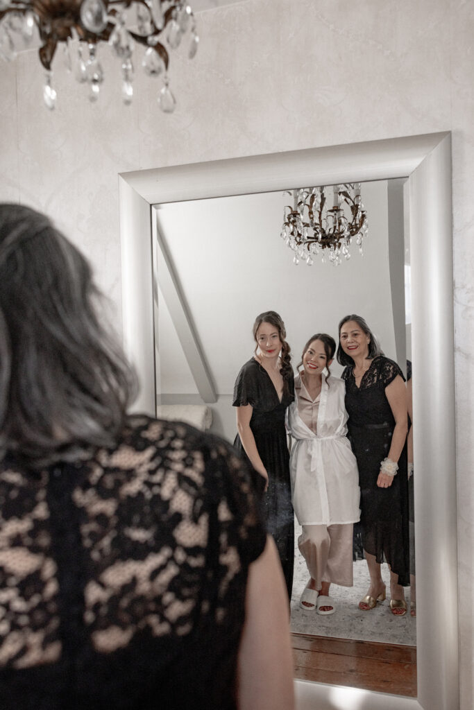 Bride standing in front of mirror with her daughter and mom. 