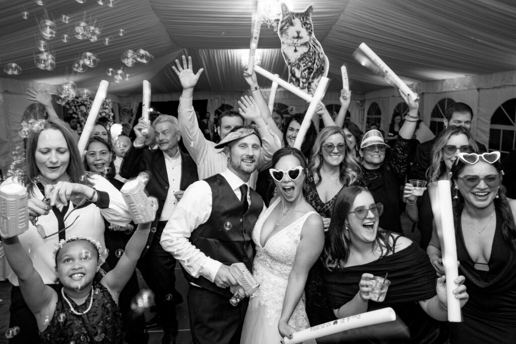 Wedding reception of everyone dancing with glow sticks, bubble gun blowing, heart shaped sunglasses and giant cat cut outs.