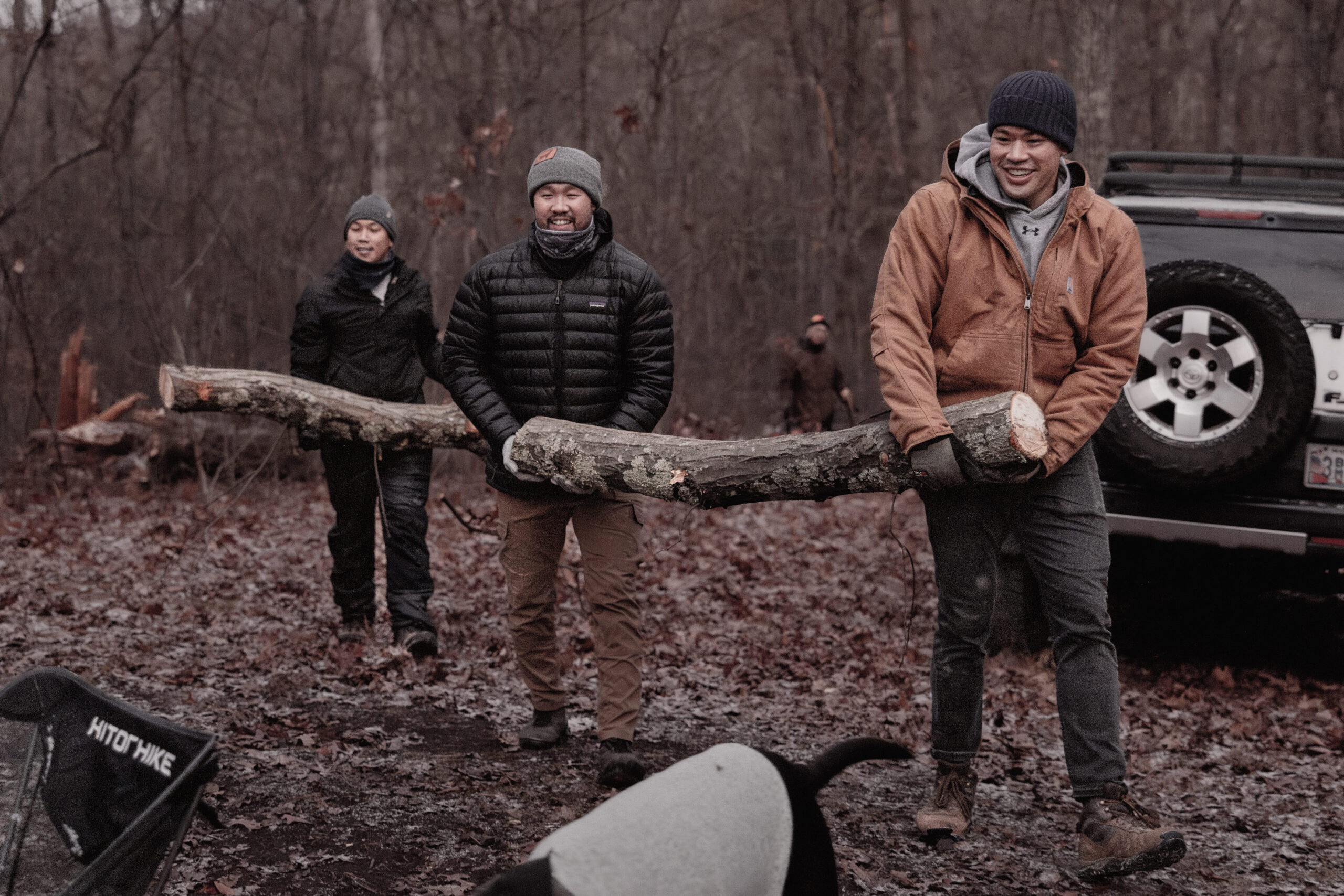 Three man carring big log to campsite for fire.