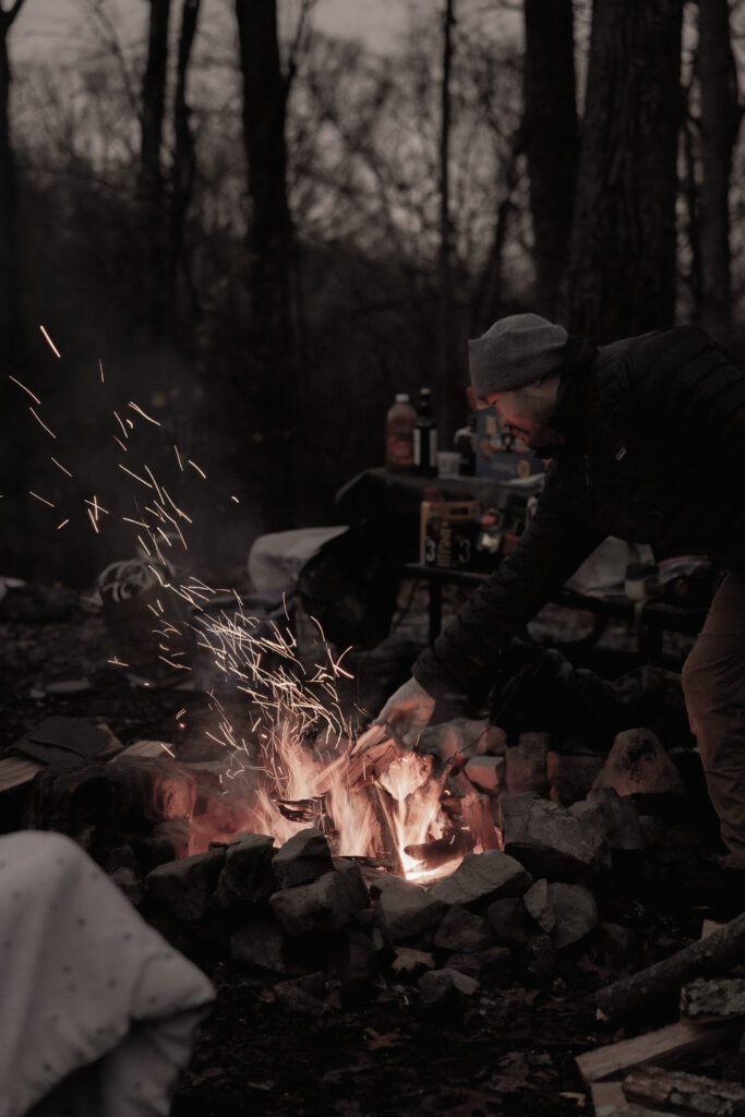 Man putting firewood into fire with amber flying off to the side.