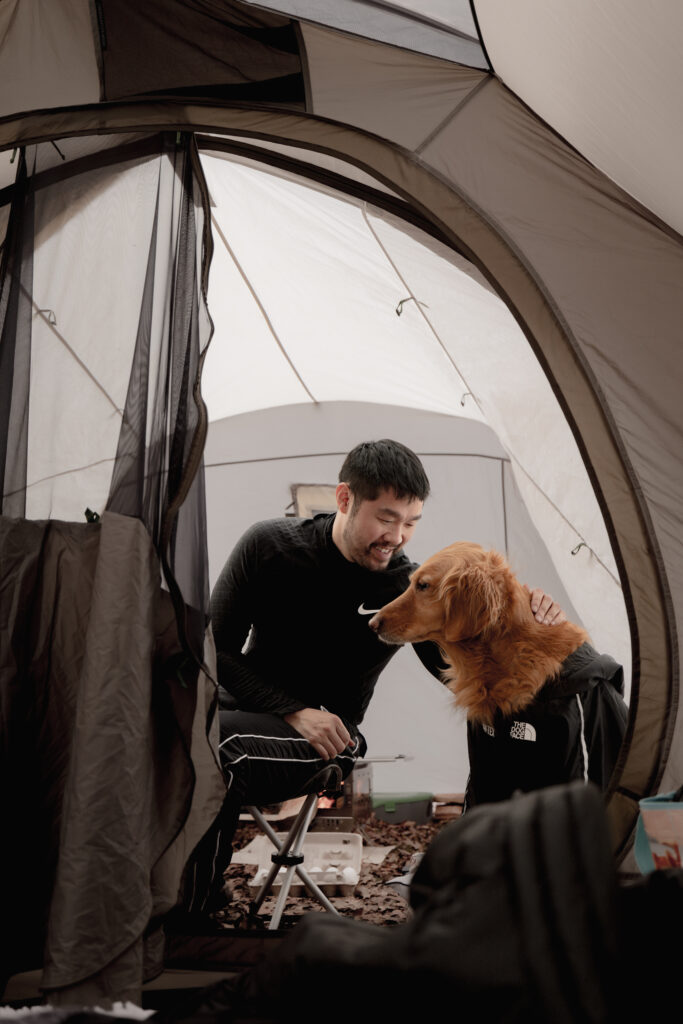 Man inside tent petting his golden retriever dog camping in winter