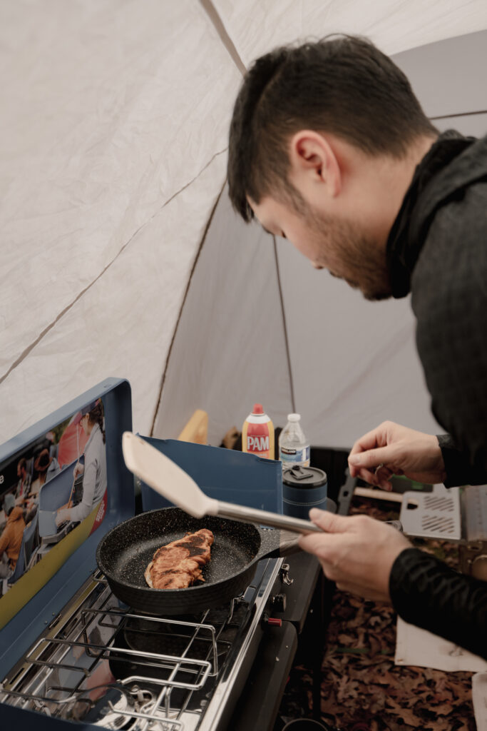 Man heating up a croissant on a camping cooker inside tent.