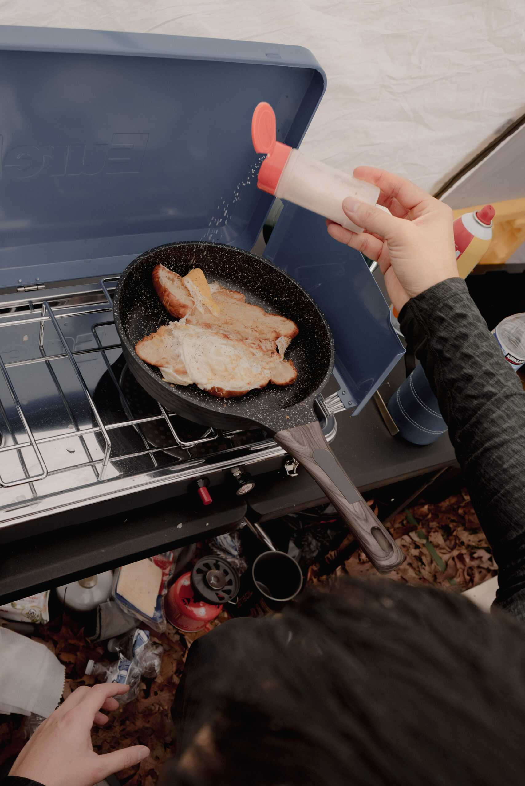 Man putting salt on food on pan cooking inside tent.